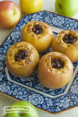 Four cored apples filled with cranberries, butter and brown sugar are baked, broiled and displayed on a serving plate.