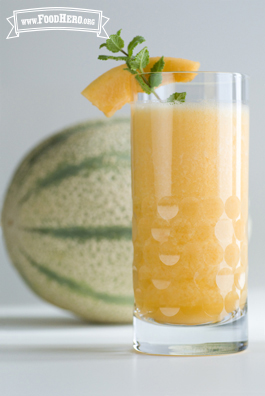 Glass filled with a bright orange juice drink garnished with mint.