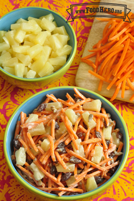 Bowl of shredded carrots with pineapples and raisins in a yogurt dressing.