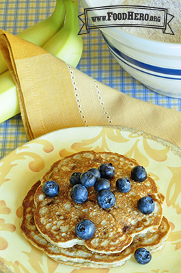 Two golden brown banana pancakes are topped with fresh blueberries.