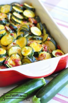 Baking dish with layers of zucchini rounds coated with tomatoes and cheese.
