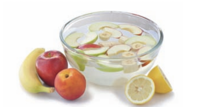 Cut apples, bananas, and lemons in a bowl of water with whole apples, bananas, and lemons next to the bowl.  