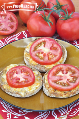 Plate of english muffin halves with cheese and a tomato slice. 