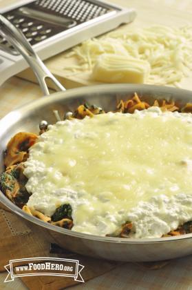 Skillet full of noodles, beef and vegetables under a layer of melted mozzarella cheese. 