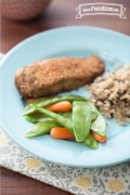 Baby carrots and snow peas on a plate with rice and fish.