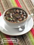 A bowl of warming soup with black beans and vegetables, garnished with herbs.