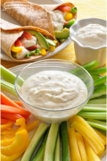 Tazón pequeño con dip cremoso con un plato de rodajas de verduras y servido en un wrap.