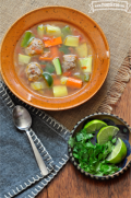 Bowl of meatballs, rice and vegetable soup served with lime and cilantro.
