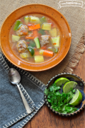 Bowl of meatballs, rice and vegetable soup served with lime and cilantro. 