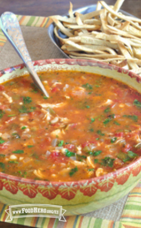 Sopa de pollo a base de tomate en un tazón grande con una guarnición de tiras de tortilla.