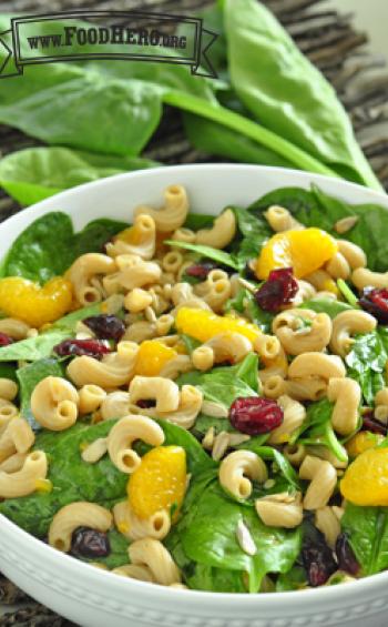 Bowl of a mix of macaroni noodles, spinach, oranges and dried cranberries.