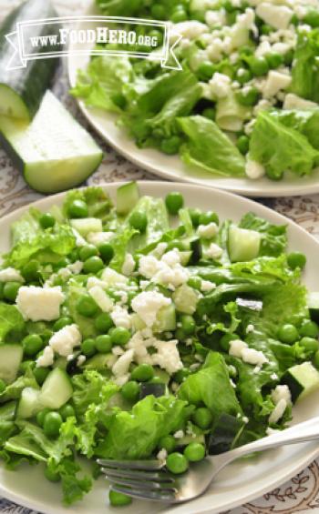 Lettuce bed topped with peas and feta cheese on a plate.