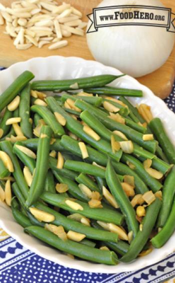 Oval serving dish with tender green beans and toppings. 