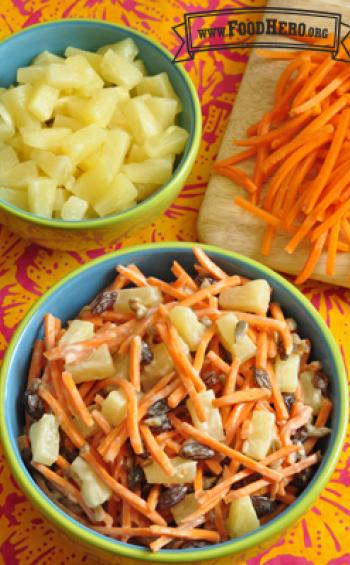 Bowl of shredded carrots with pineapples and raisins in a yogurt dressing.