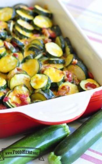 Baking dish with layers of zucchini rounds coated with tomatoes and cheese.